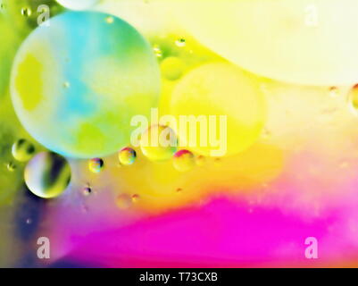 Oil drops on water surface in a glass cup with colored paper underneath. The drops are in different sizes, soft and supple. in yellow-orange, green an Stock Photo