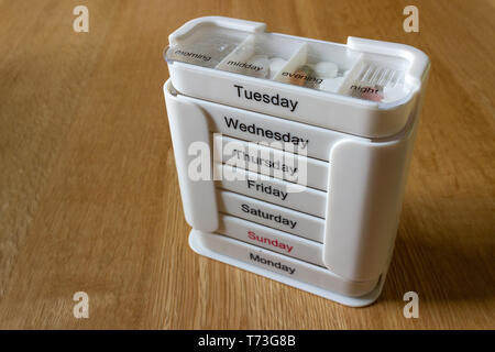White seven day four compartment medication dispenser with medication standing on an oak surface. Subject lit with natural light from front. Stock Photo