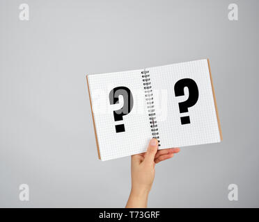 female hand holds open  notepad into a cell on gray background, question mark Stock Photo