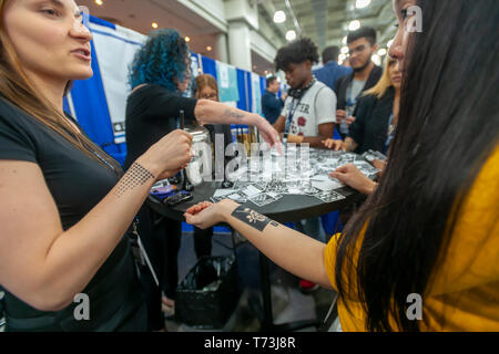 Representatives from Amkiri apply temporary tattoo stencils with fragrances at the TechDay New York event on Thursday, May 2, 2019. Thousands attended to seek jobs with the startups and to network with their peers, and perhaps to find the next big startup. TechDay bills itself as the U.S.'s largest startup event with over 350 exhibitors and over 20,000 attendees. (Â© Richard B. Levine) Stock Photo