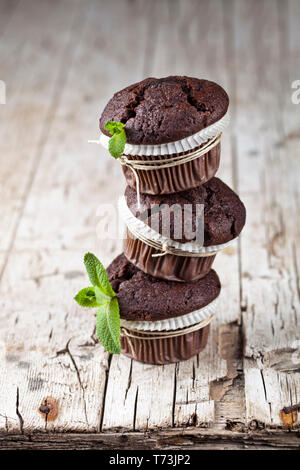 Three fresh dark chocolate muffins with mint leaves on rustic wooden table. Stock Photo