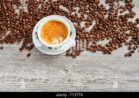 Cup of delicious hot frothy espresso coffee with scattered brown roasted beans viewed top down on rustic weathered wood with copy space below Stock Photo