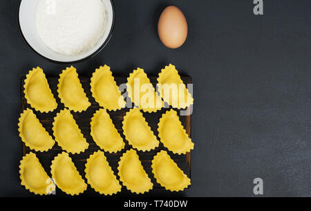 Creative layout made of uncooked ravioli pasta,flour in the bowl and one egg . Horizontal orientation with copy space. Food concept. Stock Photo