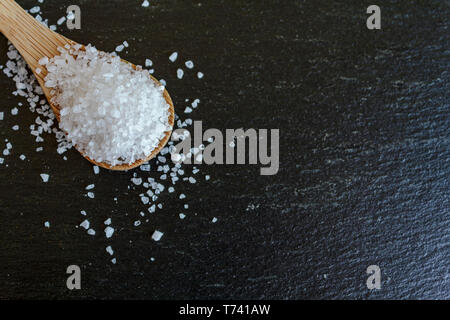 Top view of spoon with coarse grained sea salt on black background with copy space Stock Photo