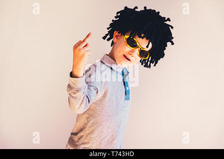 Child dressed up in funny wig showing middle finger to laugh, isolated white background. Stock Photo