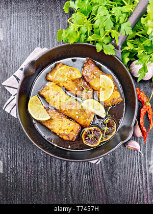 Pink salmon with honey, lemon juice, garlic, hot pepper and soy sauce, lemon slices and a sprig of thyme in frying pan on a napkin, parsley on black w Stock Photo