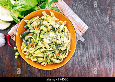 Tagliatelle pasta with zucchini, green peas, asparagus beans, hot pepper and spinach in a plate on napkin, garlic, fork and basil on wooden board back Stock Photo