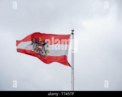 Austrian Flag with the Federal Eagle Coat of Arms and Red, White and Red Colors flying on a Grey Background Stock Photo