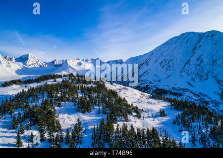 A landscape of clouds forming over Kickstep and Tincan Peaks in the backcountry of Turnagain Pass in South-central Alaska on a sunny winter day Stock Photo