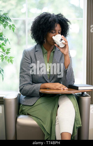 Black African American female as an adult student drinkling coffee before reading a book to study.  The intelligent woman can also be a teacher gettin Stock Photo