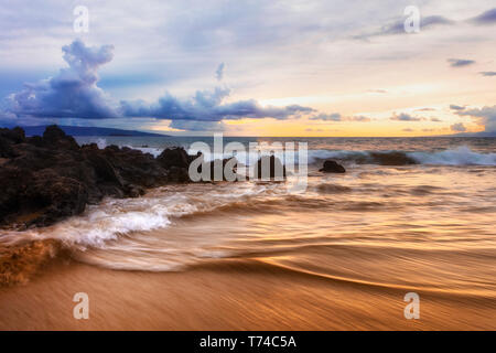 Dramatic beach sunset with soft water and lava rocks; Makena, Maui, Hawaii, United States of America Stock Photo