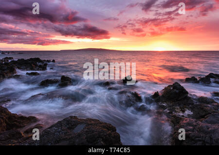 Soft water over lava rocks with a red sunset; Makena, Maui, Hawaii, United States of America Stock Photo