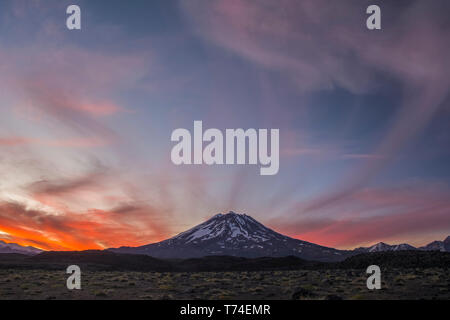 The snow-covered slopes of a volcano are set against a red sunset sky; Mendoza, Argentina Stock Photo