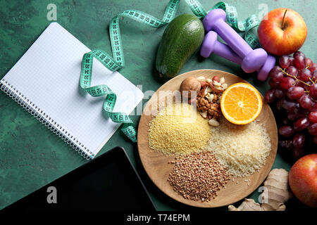 Wooden tray with healthy food and tablet PC on green background