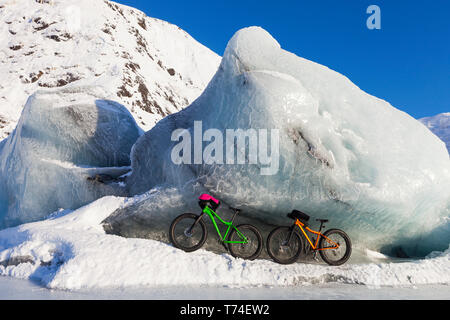 Fatbikes, 907 fat tire bike and Fatback fat tire bike, resting against giant iceberg in winter on Portage Lake, Chugach National Forest Stock Photo