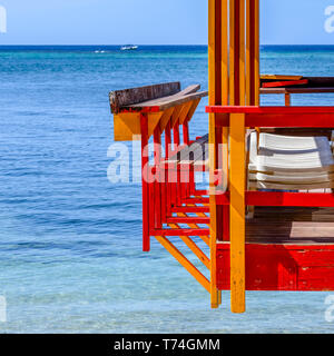 Colourful painted dock with lounge chairs and the Caribbean Sea with a boat in the distance; Roatan, Bay Islands Department, Honduras Stock Photo