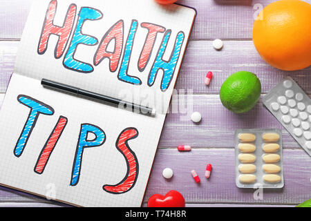 Phrase "Health tips" written in notebook with pills on wooden background Stock Photo