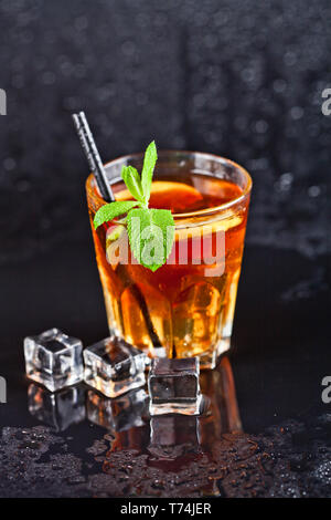 Traditional fresh iced tea with lemon, mint leaves and ice cubes in glass on wet black background. Stock Photo