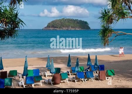 Early morning view of  Kata Yai Beach, Phuket, Thailand, with yet unoccupied beach chairs, beach umbrellas and two tourists Stock Photo