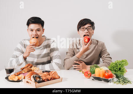 Fat upset with trays with food on white table. Unhealthy lifestyle concept. Sitting man. Two men. Tray with burgers. Man with overweight. Healthy and  Stock Photo