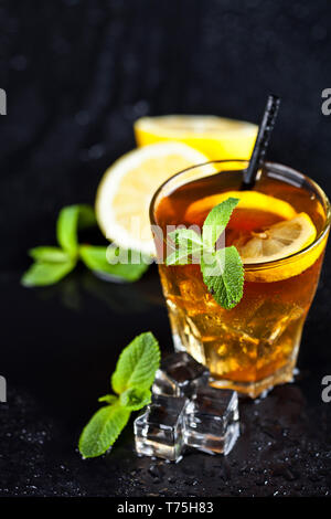 Traditional iced tea with lemon, mint leaves and ice cubes in glass on wet black background. Stock Photo