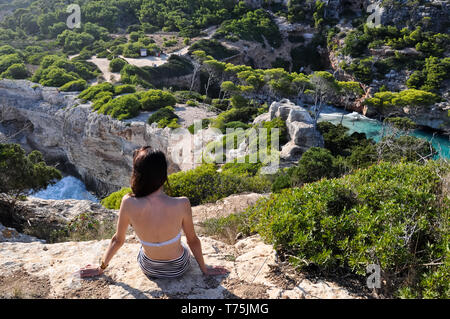 A young beautiful girl is sitting on the rock, back view. Stock Photo