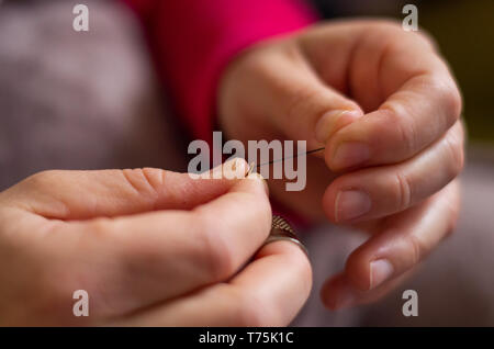 Woman cutting and knotting a thread on a needle before sewing Stock Photo