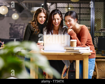 three happy businesswomen asian and caucasian using laptop computer together. Stock Photo