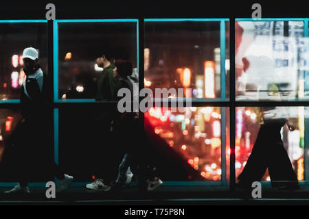 Silhouette of commuter crossing the overpass bridge of a metro station along the Wenhu line (Brown Line) during the night with bokeh from city light. Stock Photo