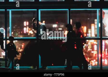 Silhouette of commuter crossing the overpass bridge of a metro station along the Wenhu line (Brown Line) during the night with bokeh from city light. Stock Photo