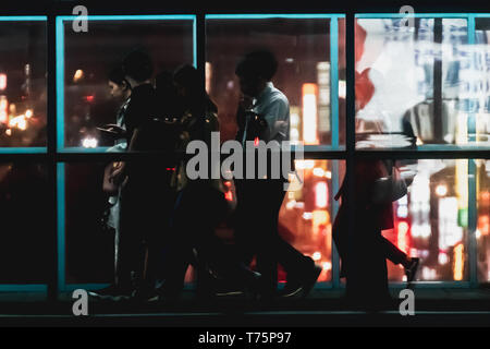 Silhouette of commuter crossing the overpass bridge of a metro station along the Wenhu line (Brown Line) during the night with bokeh from city light. Stock Photo