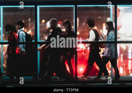 Silhouette of commuter crossing the overpass bridge of a metro station along the Wenhu line (Brown Line) during the night with bokeh from city light. Stock Photo