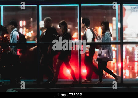 Silhouette of commuter crossing the overpass bridge of a metro station along the Wenhu line (Brown Line) during the night with bokeh from city light. Stock Photo