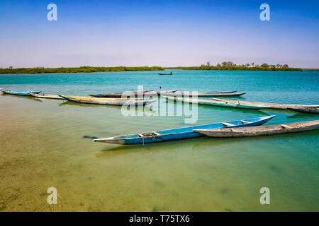 Wooden canoe on sea lagoon in Senegal in Africa. It is the Saloum National Nature Park, a bird sanctuary. In the background is blue sky and the island Stock Photo