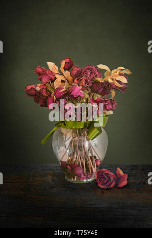 Vintage dried red roses flowers in a glass vase with green ribbon Stock Photo