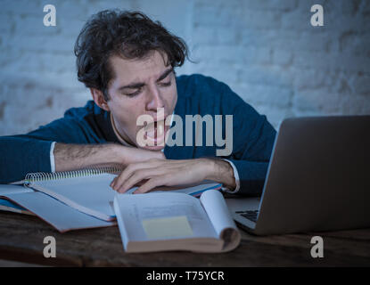 Overworked and tired male student working late at night on laptop trying not to fall asleep feeling fatigued, worried and sad. Moody dark light. Final Stock Photo