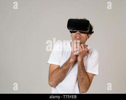 Young man using virtual reality goggles feeling excited and shock exploring virtual world making scared gestures having a scary VR adventure. Innovati Stock Photo