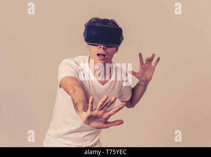 Young man using virtual reality goggles feeling excited and shock exploring virtual world making scared gestures having a scary VR adventure. Innovati Stock Photo