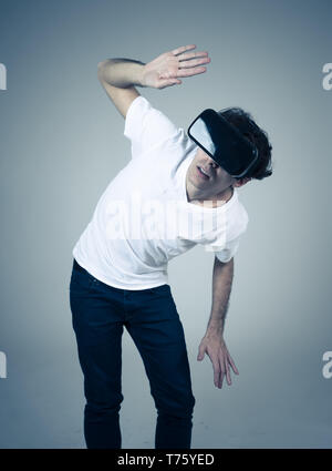 Young man using virtual reality goggles feeling excited and shock exploring virtual world making scared gestures having a scary VR adventure. Innovati Stock Photo