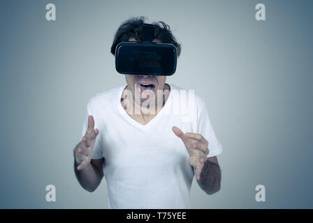 Young man using virtual reality goggles feeling excited and shock exploring virtual world making scared gestures having a scary VR adventure. Innovati Stock Photo
