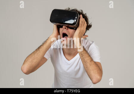 Young man using virtual reality goggles feeling excited and shock exploring virtual world making scared gestures having a scary VR adventure. Innovati Stock Photo