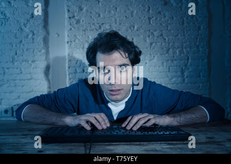 Overworked and tired male working late at night on computer trying not to fall asleep feeling fatigued and overworked. lifestyle portrait in Moody dar Stock Photo
