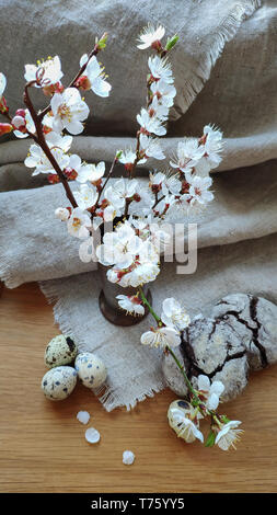 Beautiful white flowering branch of apricots in a vase on a natural fabric and light wooden surface and brownie cookies with quail eggs, Easter concep Stock Photo
