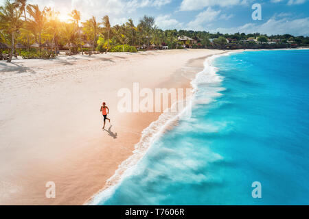 Aerial view of the running young woman on the white sandy beach near sea with waves at sunset. Summer holiday. Top view of sporty slim girl, clear azu