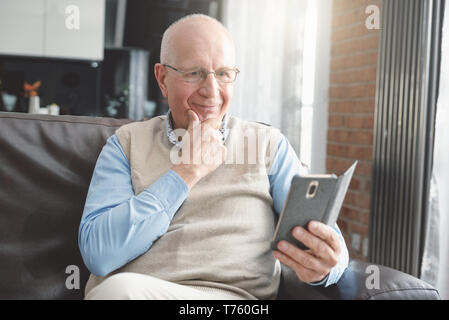 Senior man using a smartphone and smiling while sitting on couch at home. Stock Photo