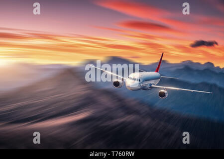 Airplane in motion. Aircraft with motion blur effect is flying over hills and mountains at sunset. Passenger airplane, blurred clouds. Passenger aircr Stock Photo