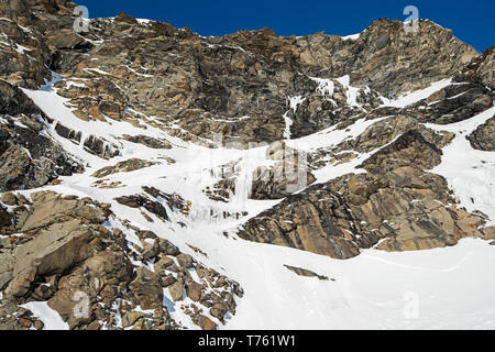 Rugged alpine rocky mountainside with frozen waterfall covered in snow and ice Stock Photo