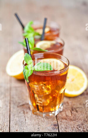Traditional iced tea with lemon, mint leaves and ice cubes in three glasses on rustic wooden table background. Stock Photo