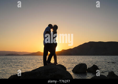 Kiss on the background of the sunset. Silhouette of a loving couple. Beautiful view of the sea and the hills Stock Photo