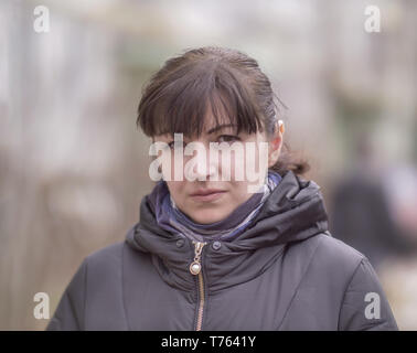 Portrait of a serious and attractive brunette girl on a blurred background of the street, looking at the camera Stock Photo